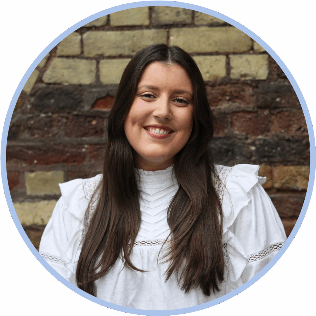 White woman with dark brown hair wearing a white top and smiling to camera