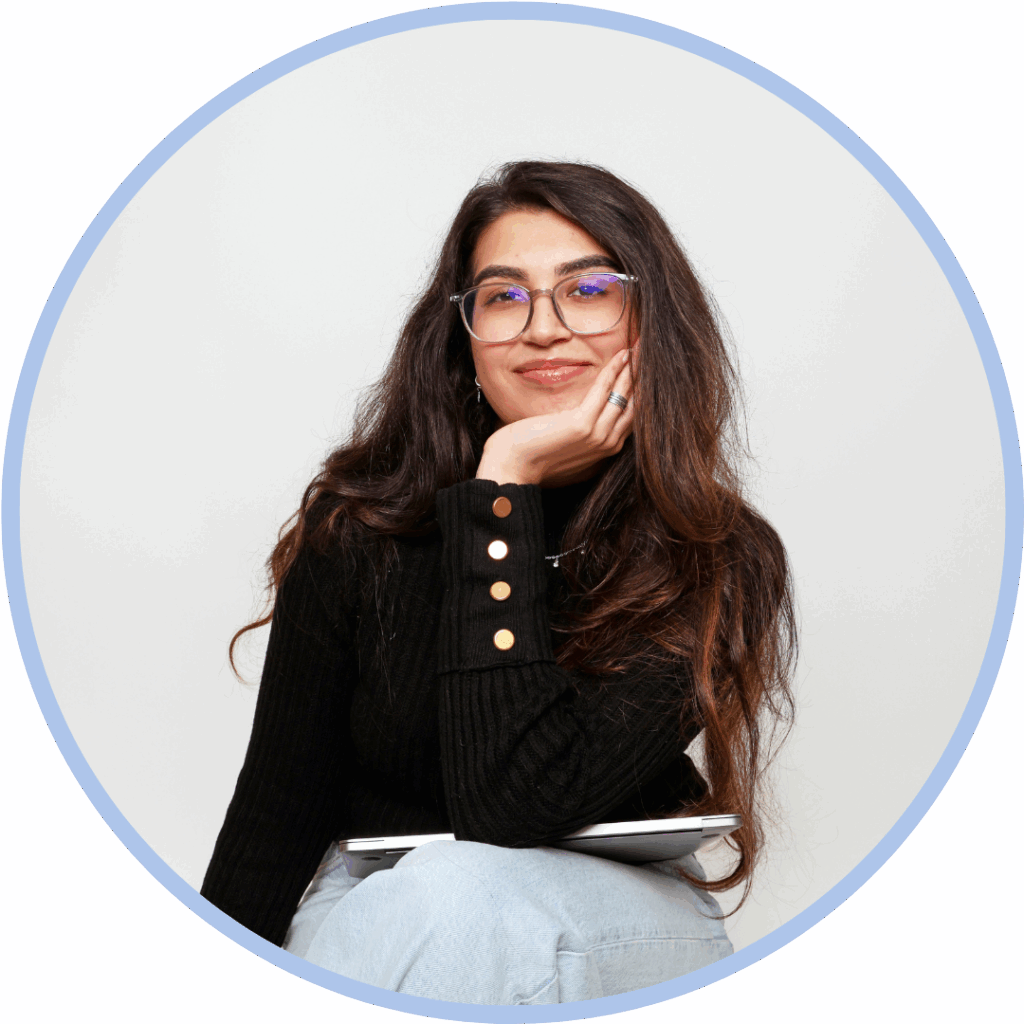 Asian woman with dark brown hair, wearing glasses leaning her chin on her hand and smiling to camera