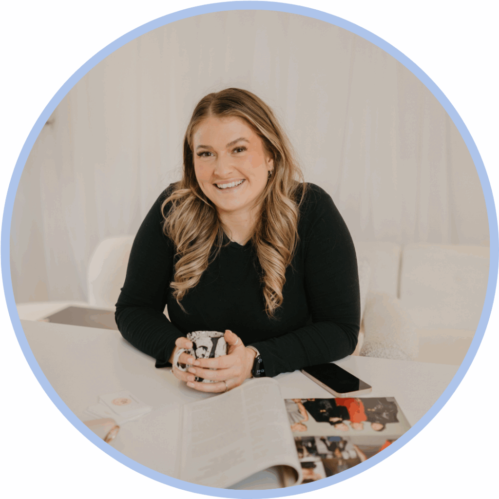 White woman with long blonde hair leaning on a desk and holding a mug smiling to camera