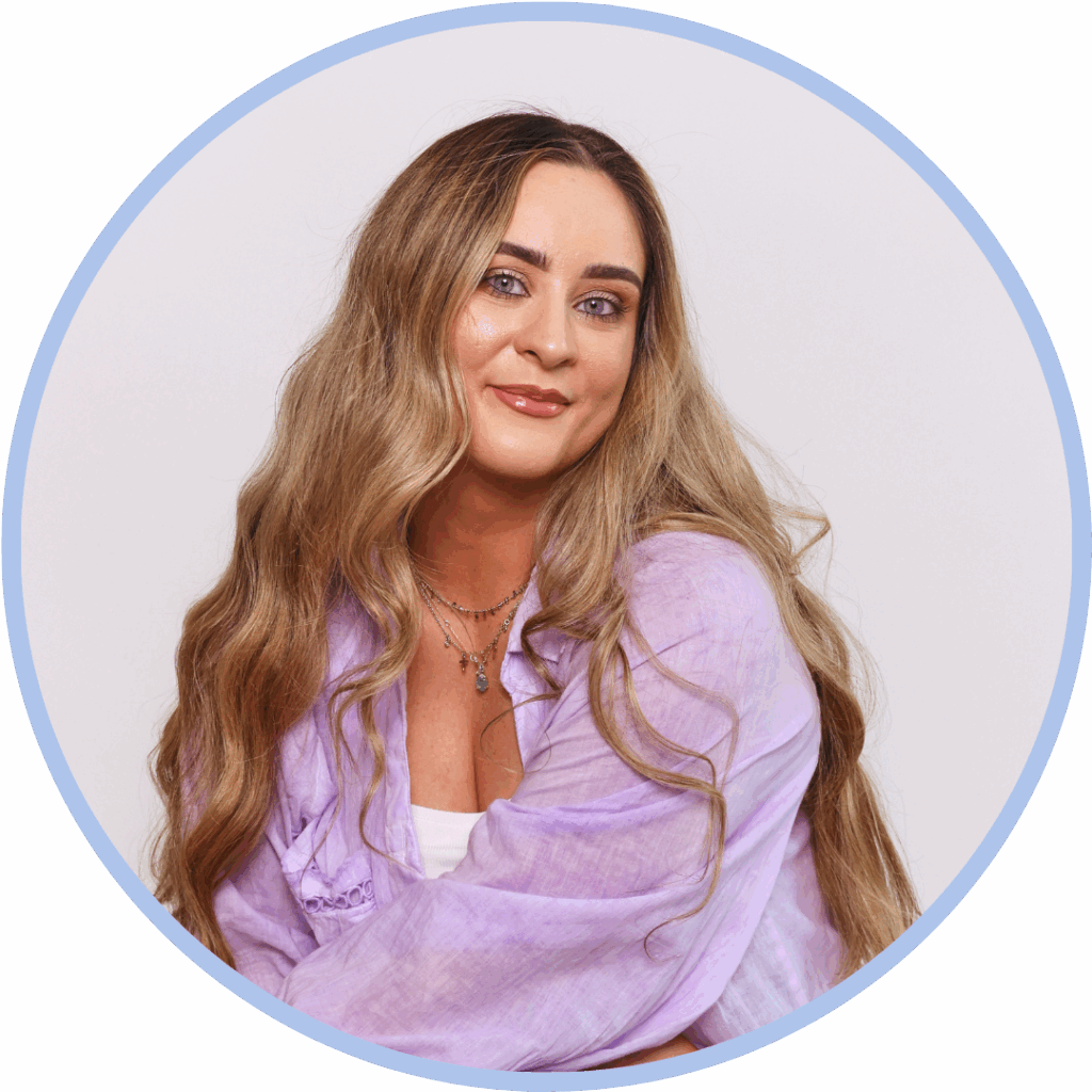 Headshot of a white woman with long blonde hair wearing a pink shirt and smiling to camera