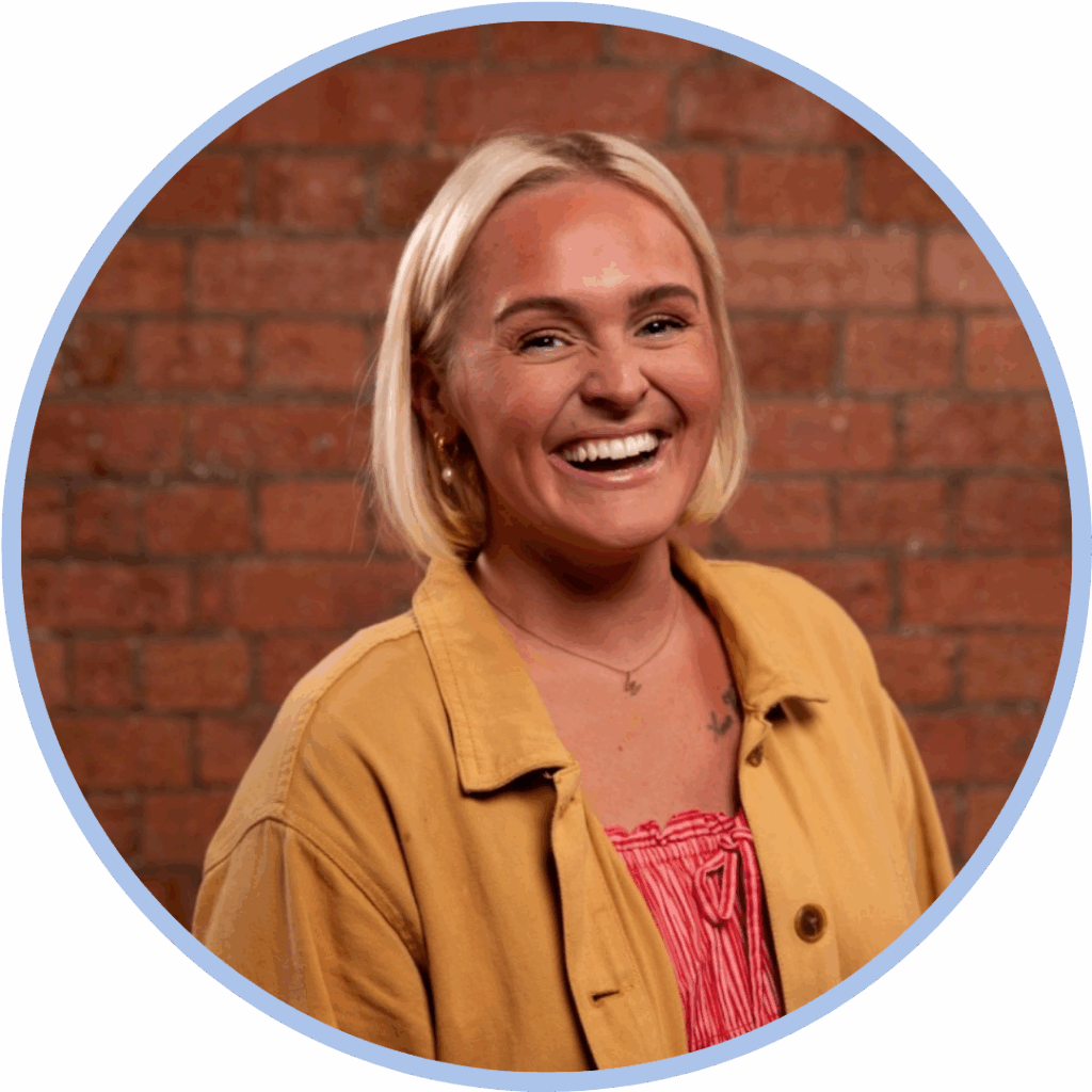 Headshot of a white woman with a blond bob wearing a yellow shirt and smiling to camera